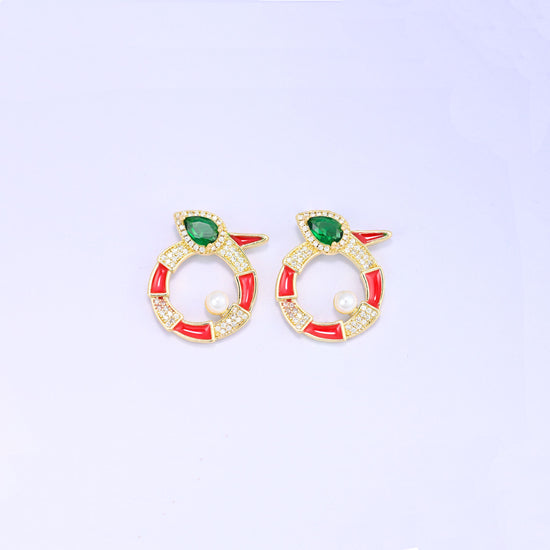 Two red round snake charms side by side, each 18K gold plated with a green pear cut stone head, zircon pave along the coil and a round pearl.