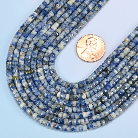 Close view of blue spot jasper faceted heishi disc strands curving beside a US penny for scale