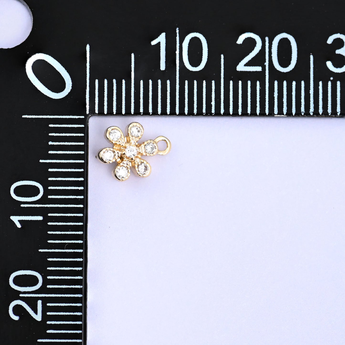 Small gold charms, one flower charm at the corner of a millimetre ruler showing the size