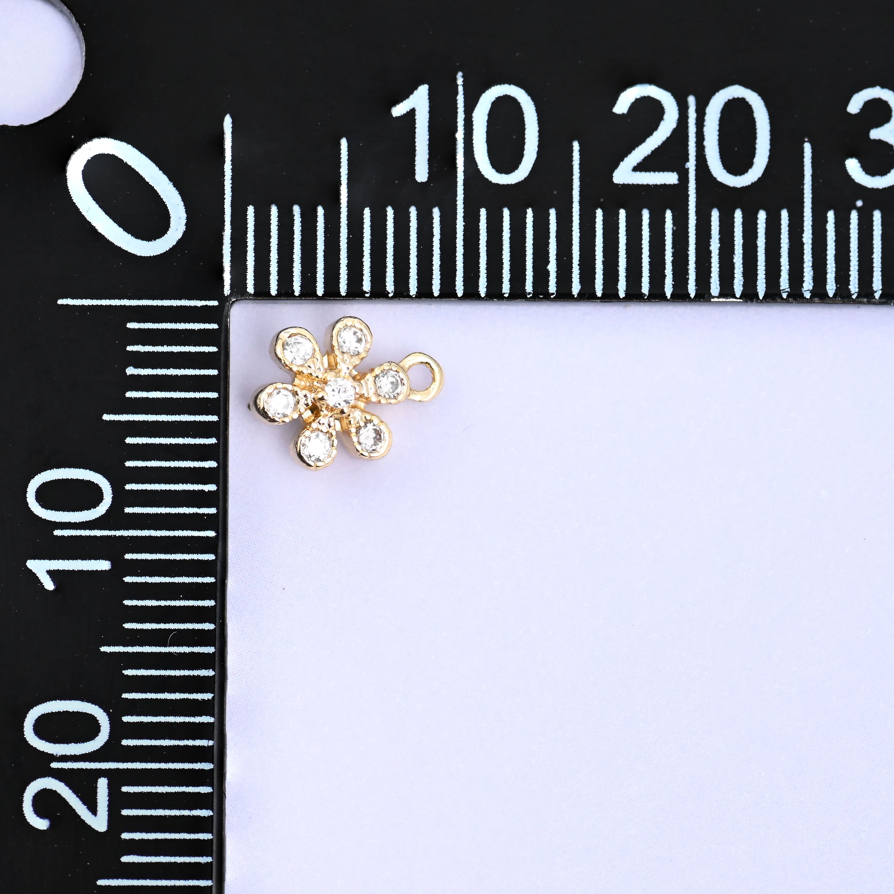 Small gold charms, one flower charm at the corner of a millimetre ruler showing the size
