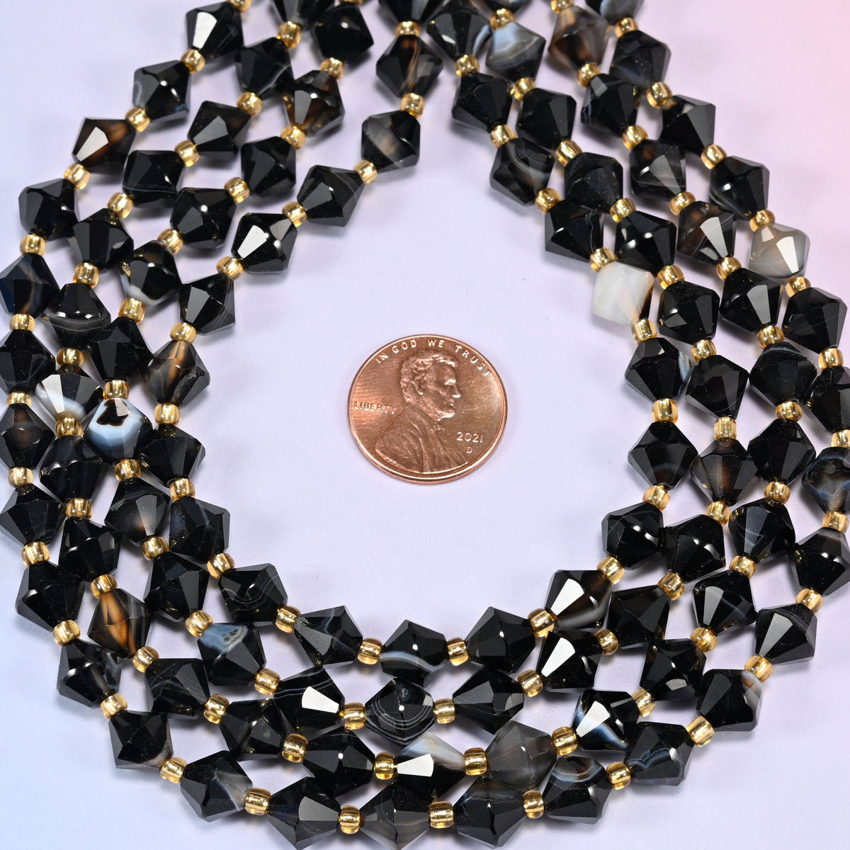 Dyed black strip agate bicone beads coiled into a ring, seen from above, high gloss running across the facets.