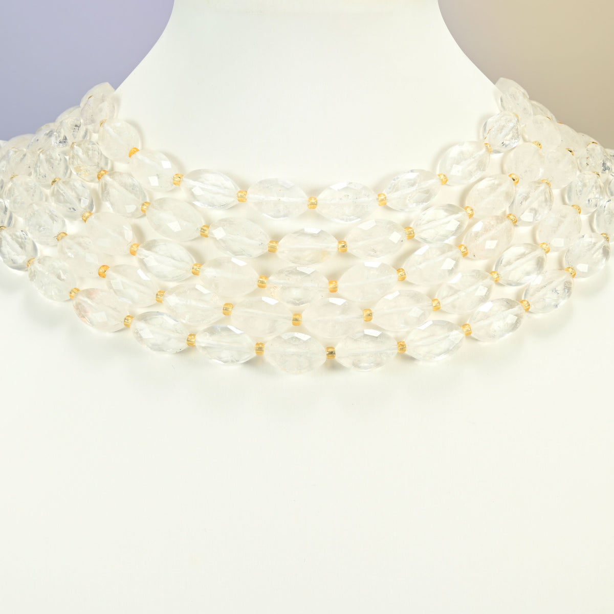 Clear quartz faceted flat oval strands arranged as a layered collar on a white display bust, clear beads across the neck