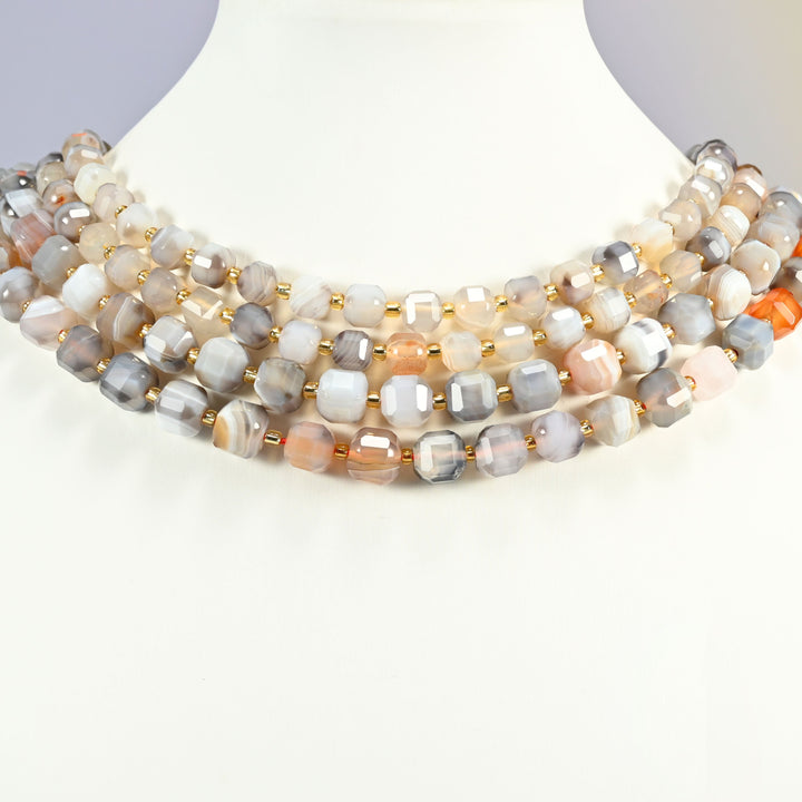 Botswana agate faceted cube strands arranged as a layered collar on a white display bust, gray, white and peach beads across the neck