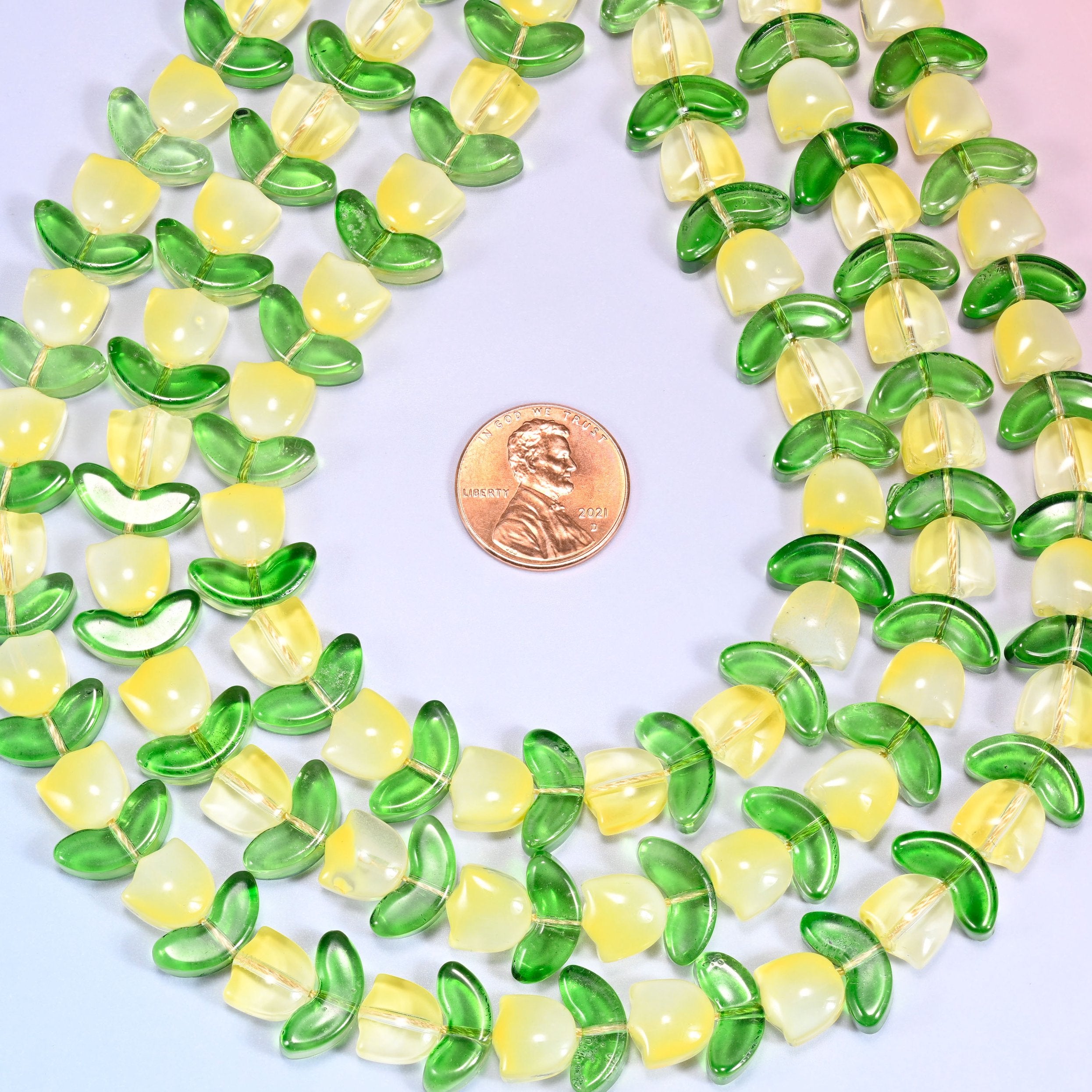 Wide view of a circular coil of yellow tulip and green leaf glass beads on a lavender background, showing the alternating pattern.