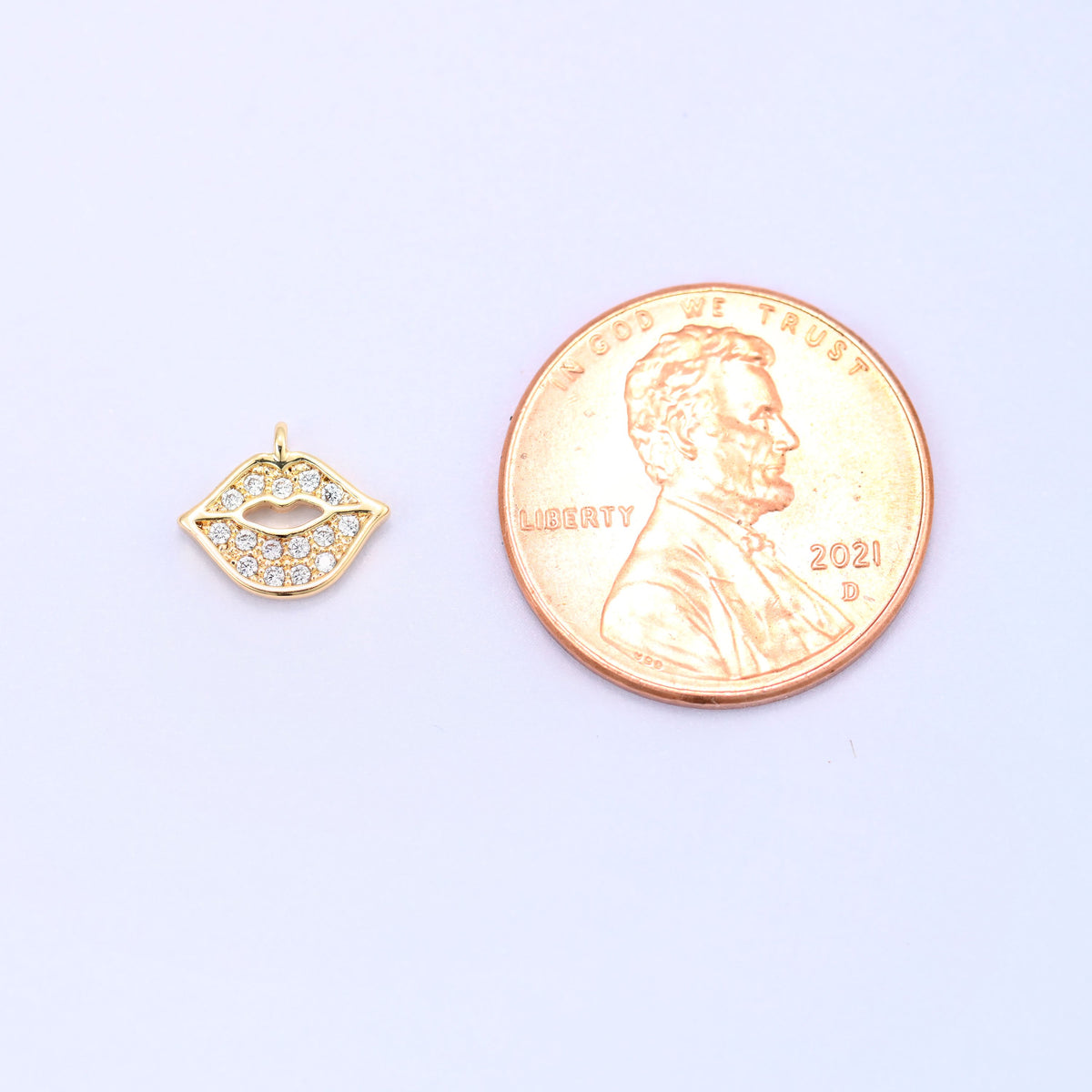 Small gold charms, one lip charm shown beside a US penny for size