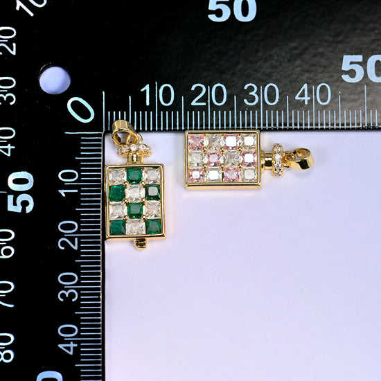 Two perfume bottle zirconia charms on a millimetre ruler, the green one upright at the zero mark and the pink one laid flat to show height and width.