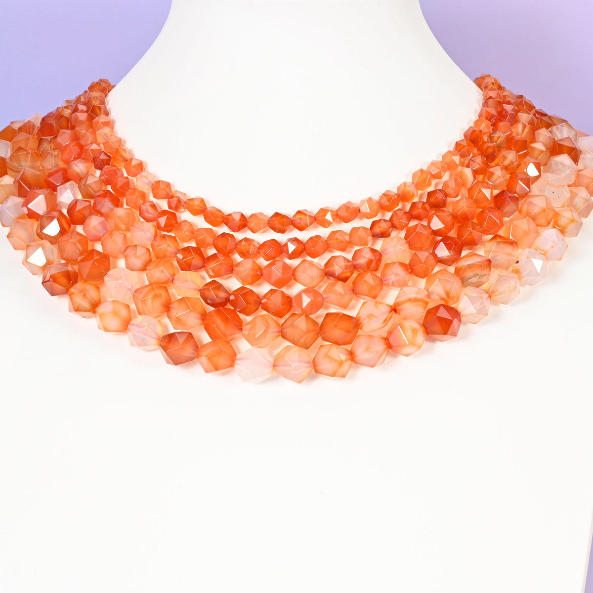 Orange Agate star cut beads looped around a white neck form, several strands sitting together as a collar