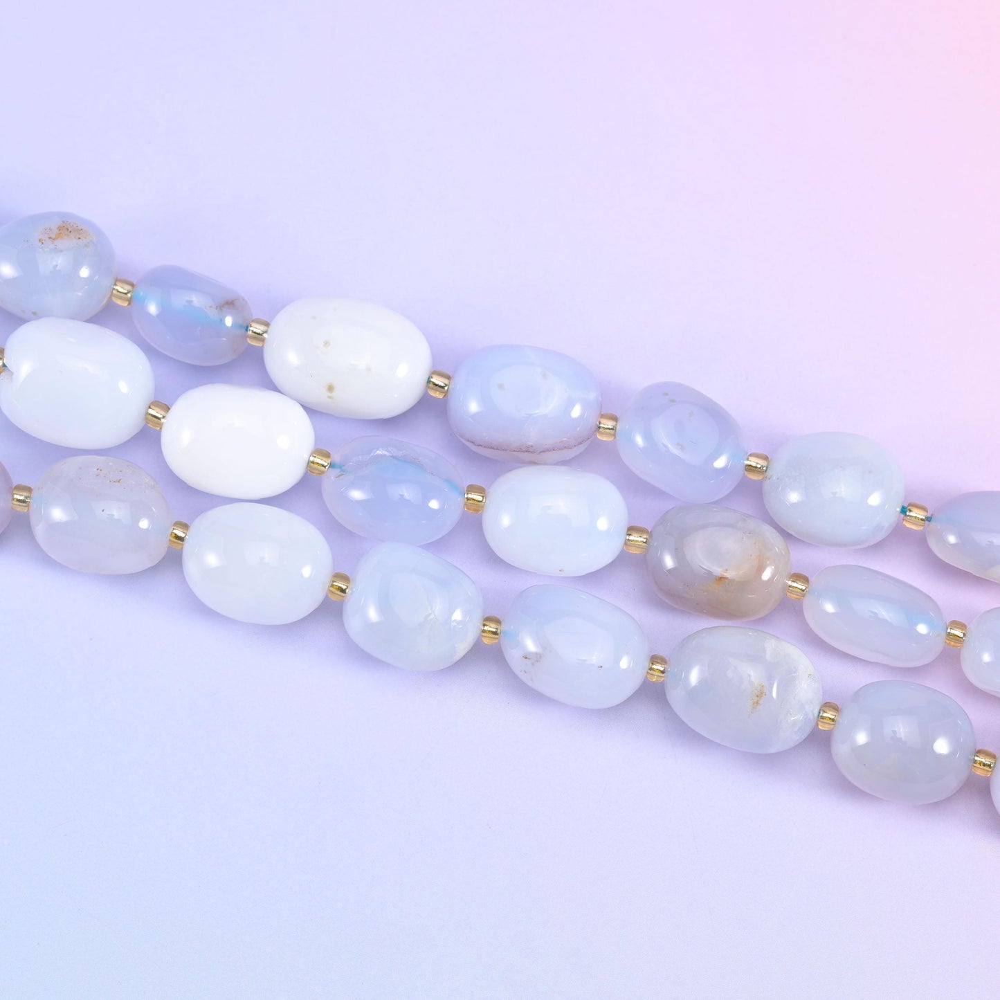 Two strands of 10-17mm chalcedony nuggets running diagonally across a pale lilac backdrop
