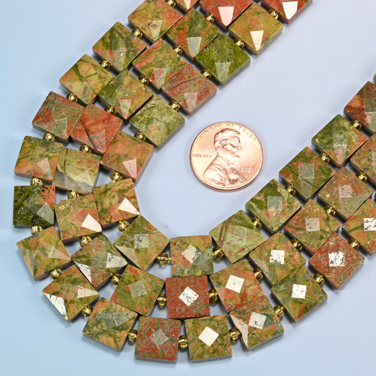 Close view of natural unakite faceted flat square strands curving beside a US penny for scale