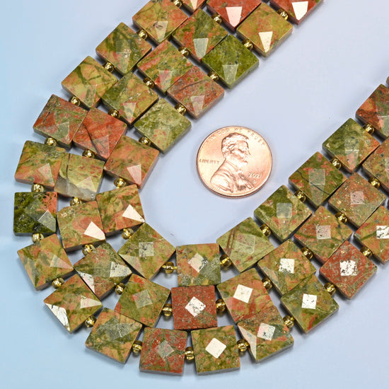 Close view of natural unakite faceted flat square strands curving beside a US penny for scale