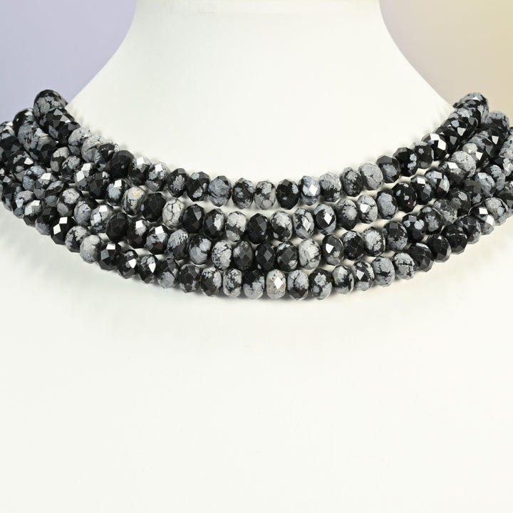Snowflake jasper faceted rondelle strands arranged as a layered collar on a white display bust, black and gray beads across the neck