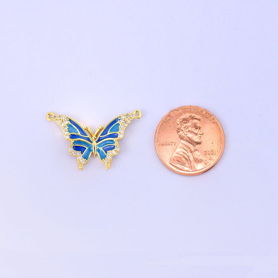 Scale shot of the enamel butterfly double connector pendant, the blue butterfly beside a US penny and noticeably wider than the coin.
