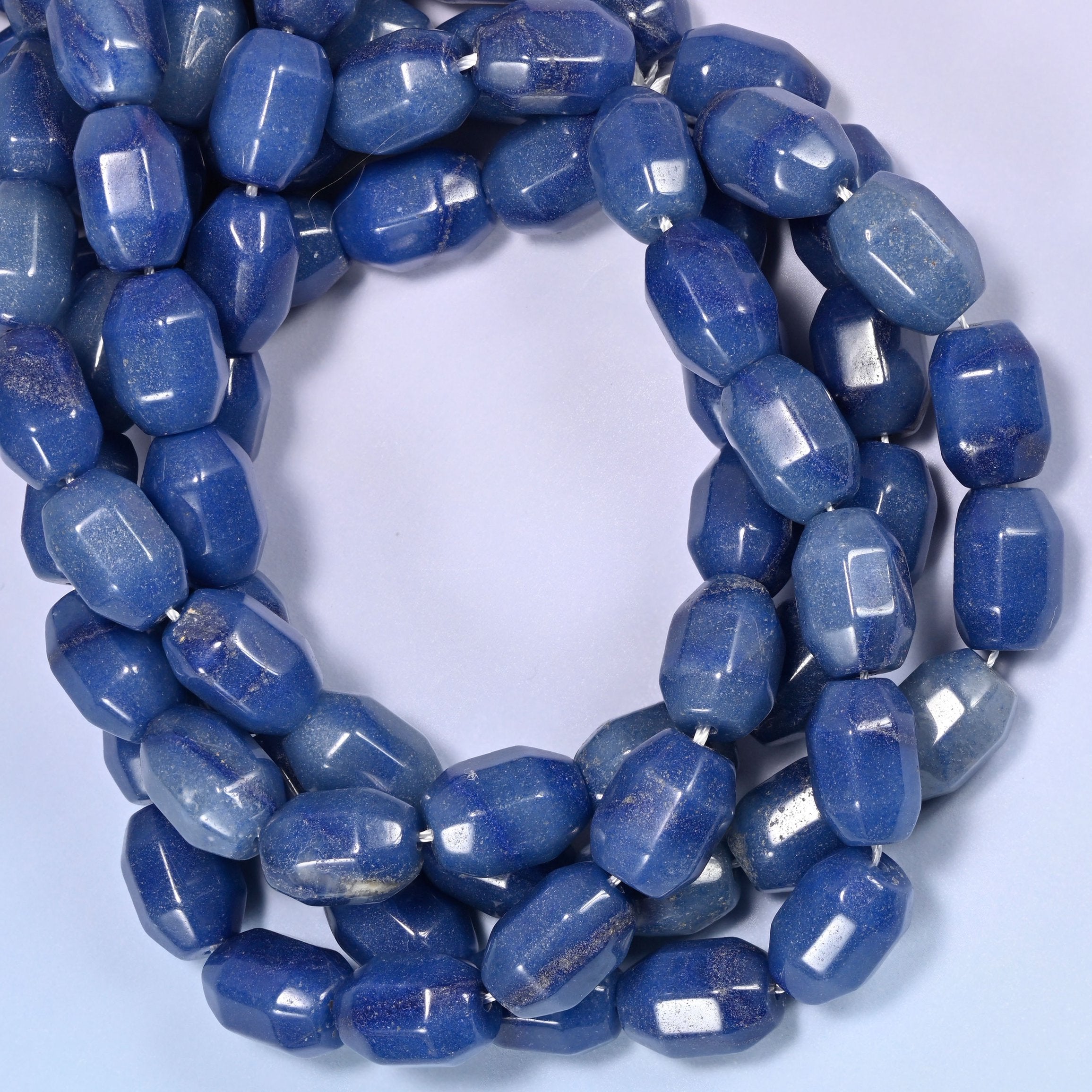 Circular coil of blue faceted Aventurine barrel bead strands on a light blue background with a penny in the center for size comparison.