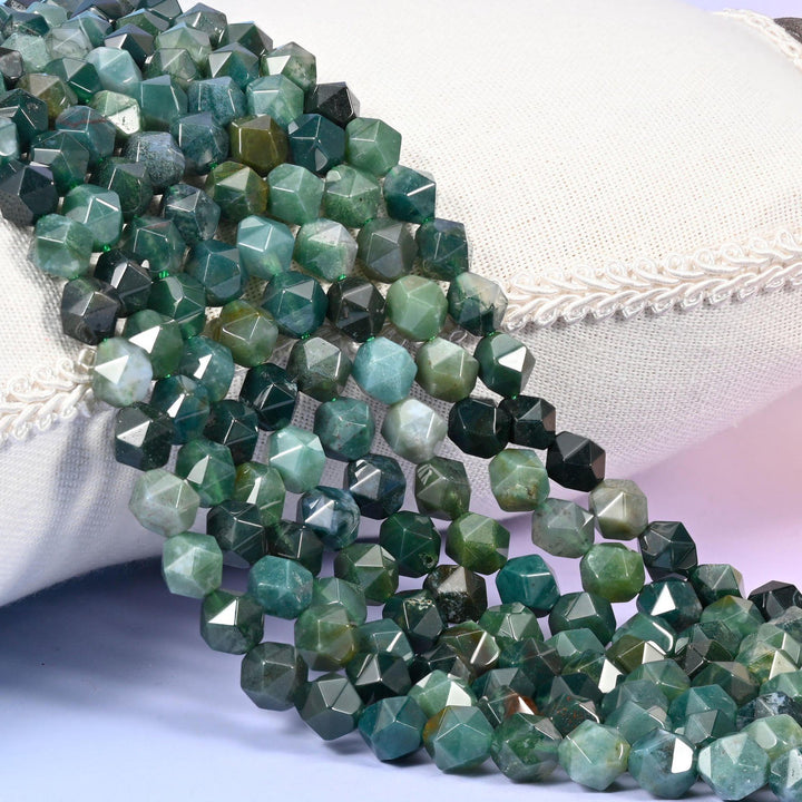 Moss Agate diamond star cut beads, strands laid over white fabric, deep mossy green with cloudy grey-white patches