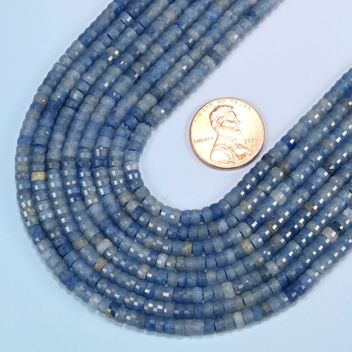 Close view of blue aventurine faceted heishi disc strands curving beside a US penny for scale