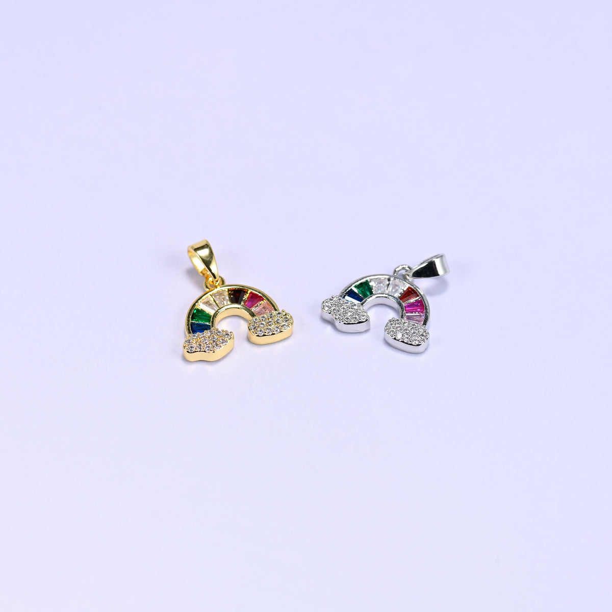 Two Rainbow Zirconia Charms angled across the frame, gold and silver tone versions showing the cloud base and side profile.