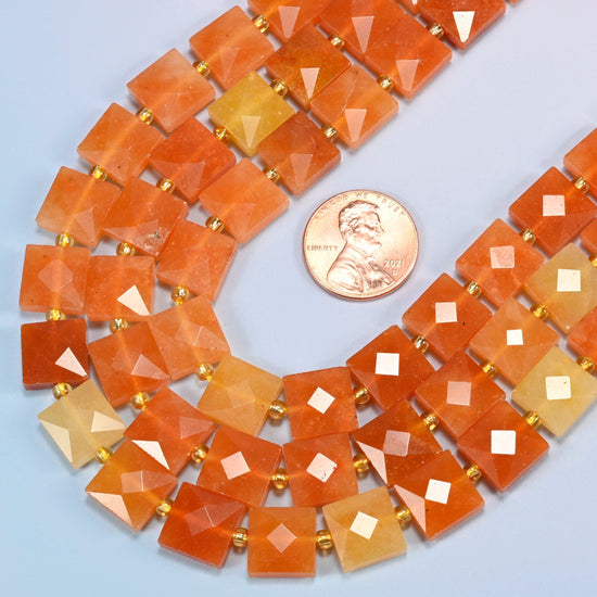 Close view of natural red aventurine faceted flat square strands curving beside a US penny for scale