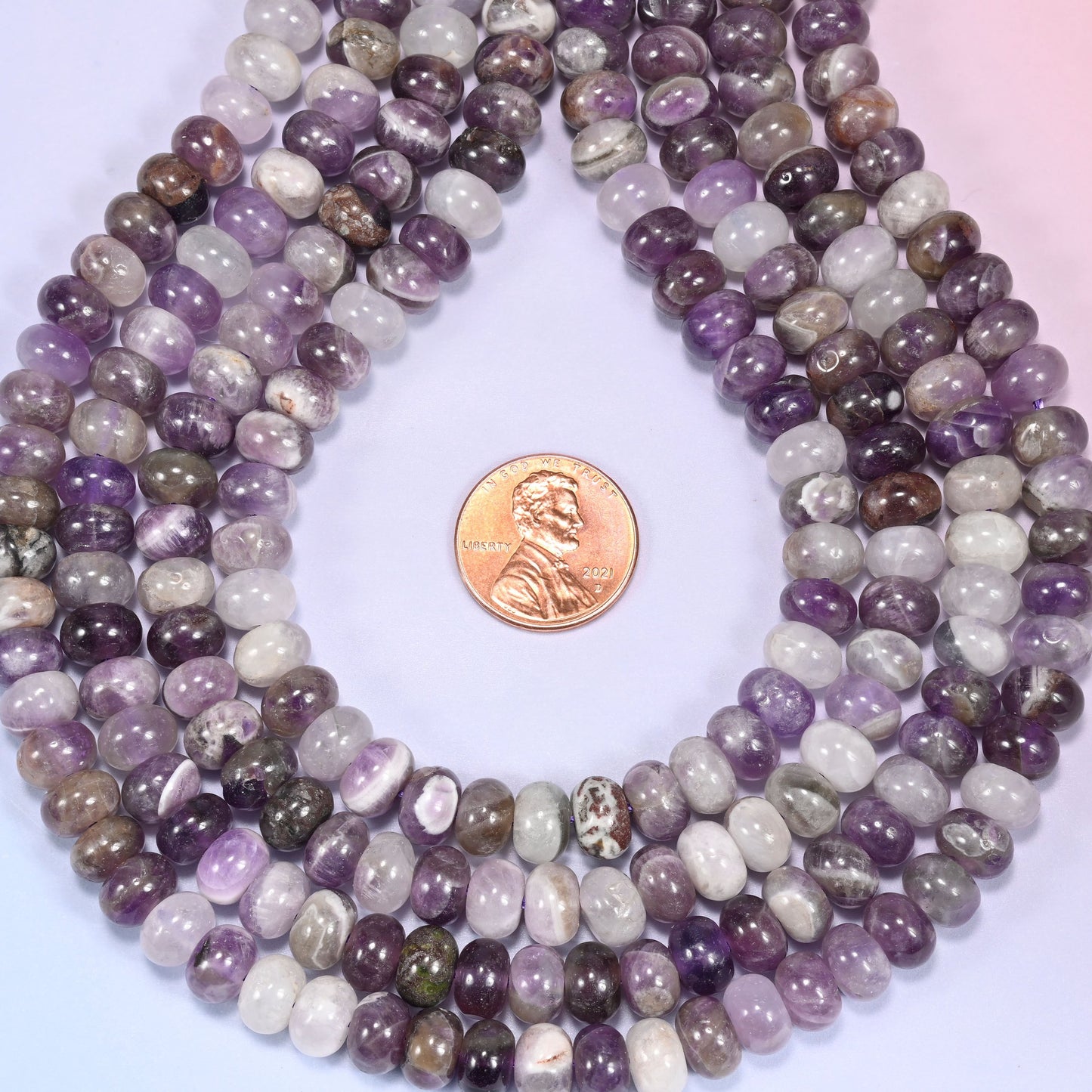 Bundled coil of Amethyst rondelle beads on a lavender background with a penny placed at the center for scale.