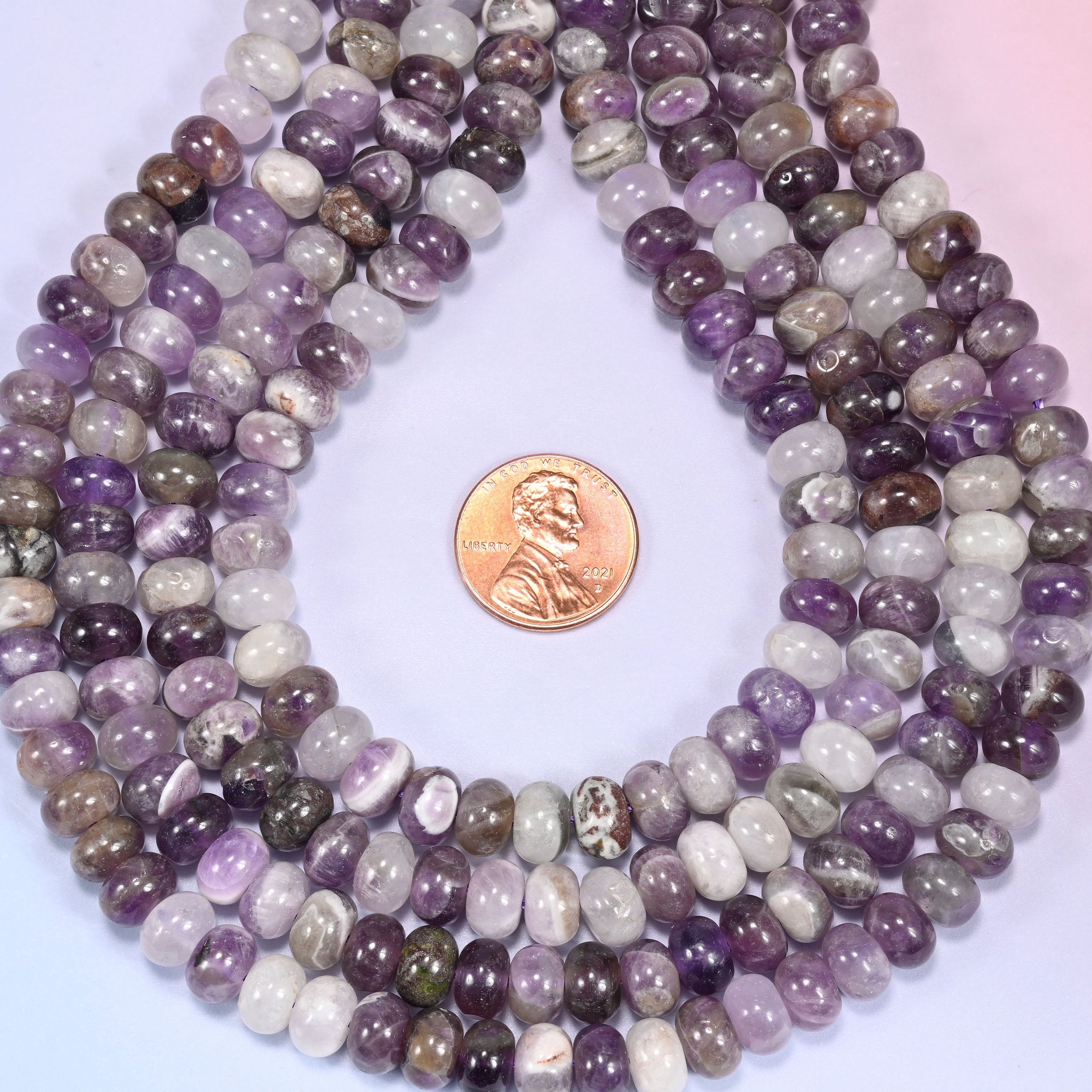 Bundled coil of Amethyst rondelle beads on a lavender background with a penny placed at the center for scale.