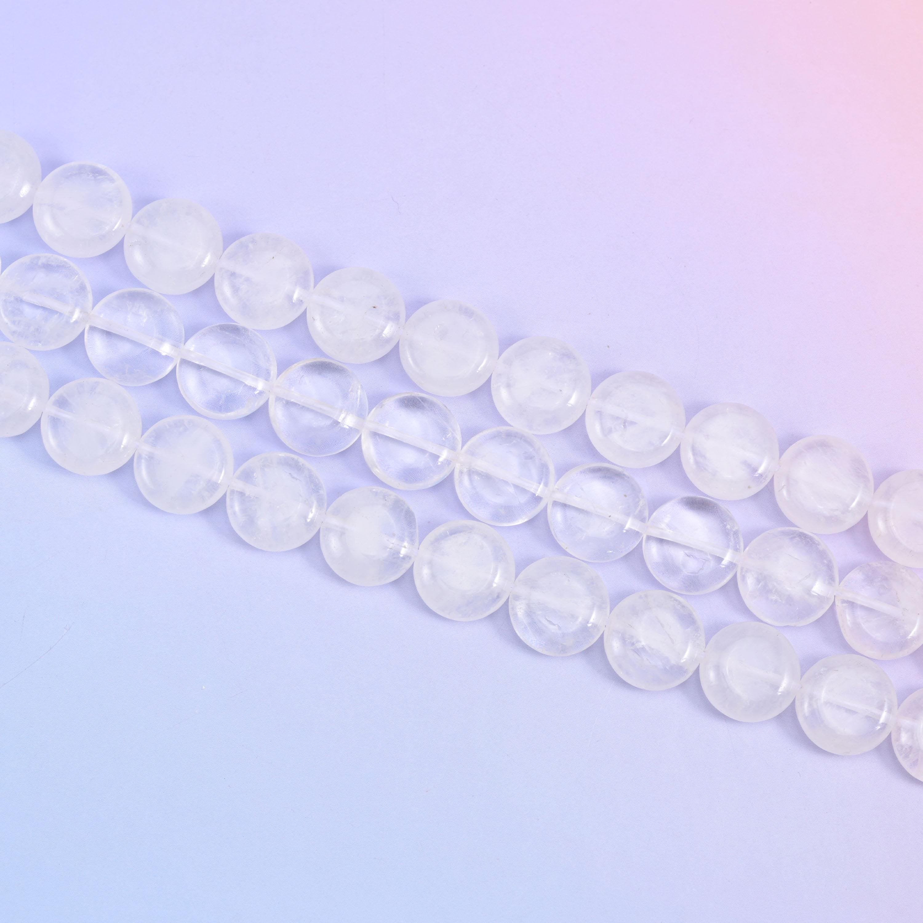 Angled run of clear quartz coins across a soft lavender surface, cloudy and transparent beads mixed