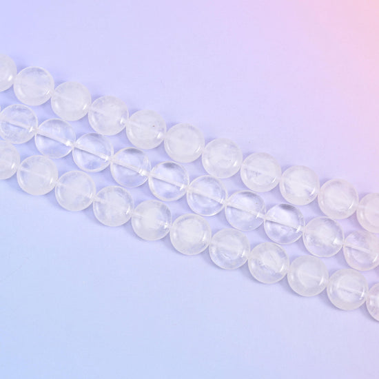 Angled run of clear quartz coins across a soft lavender surface, cloudy and transparent beads mixed