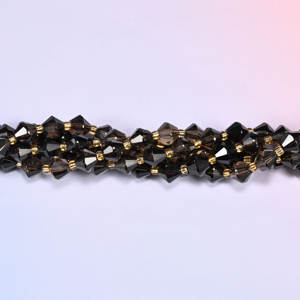 Macro close-up of 8mm Smoky Quartz faceted bicone beads on a strand, showing the faceted cut and gold-tone spacer beads.