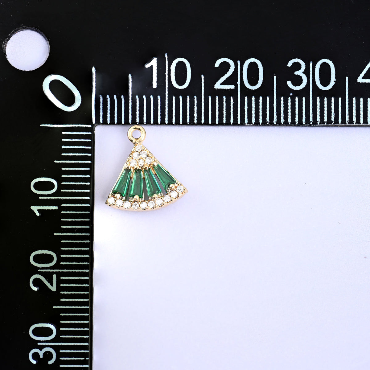 Small gold charms, one green fan charm at the corner of a millimetre ruler showing the size