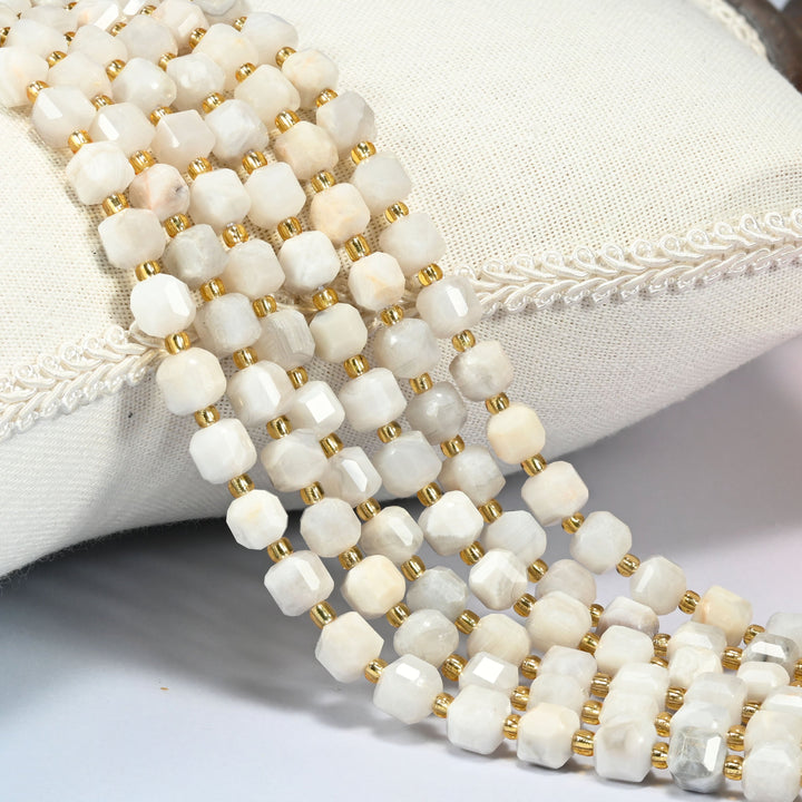 White crazy agate faceted cube beads 6mm with small gold spacer beads, several strands draped over a white cushion