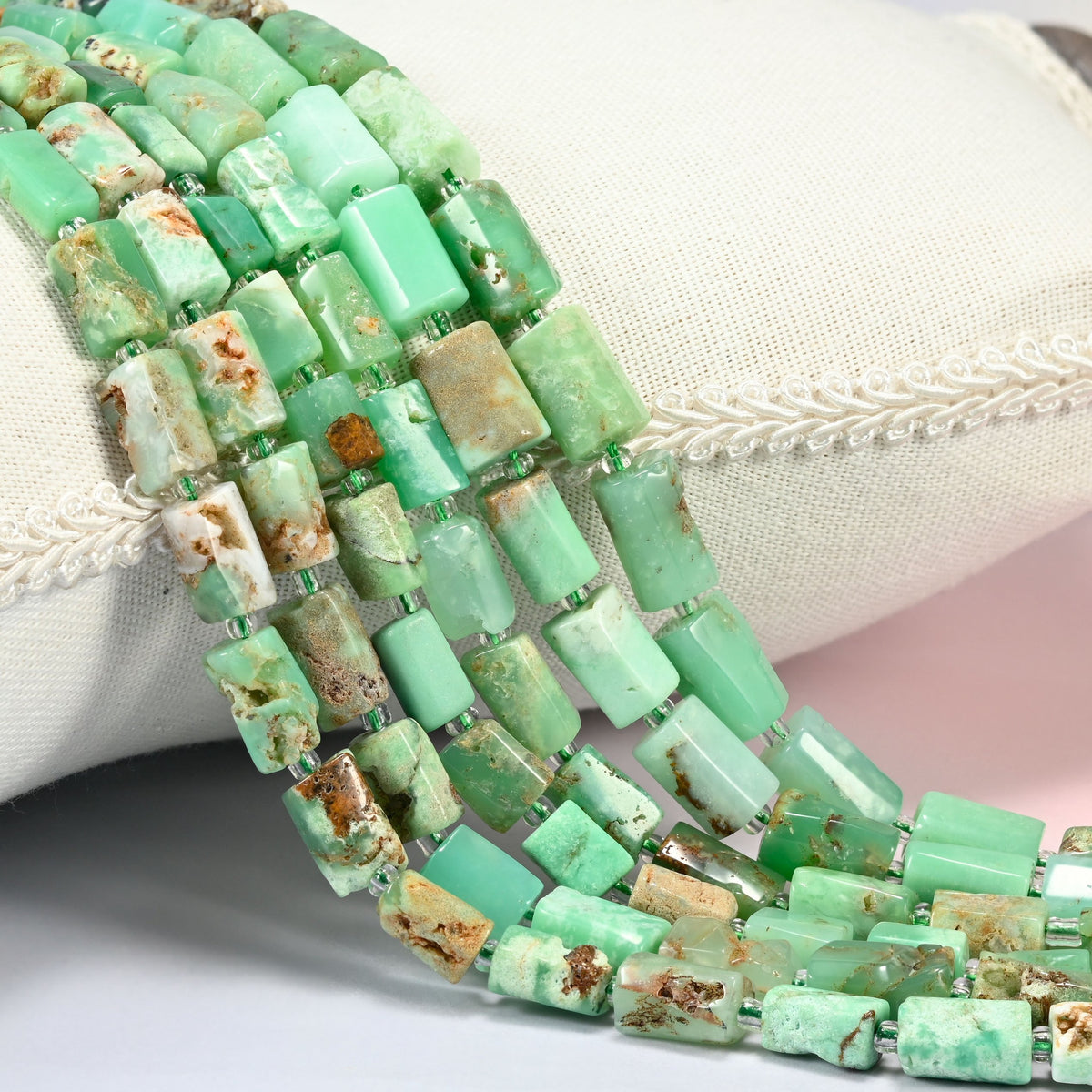 Australian jade faceted tube beads 7x9-8x12mm with small light green seed bead spacers, several strands draped over a white cushion