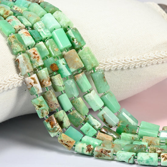 Australian jade faceted tube beads 7x9-8x12mm with small light green seed bead spacers, several strands draped over a white cushion