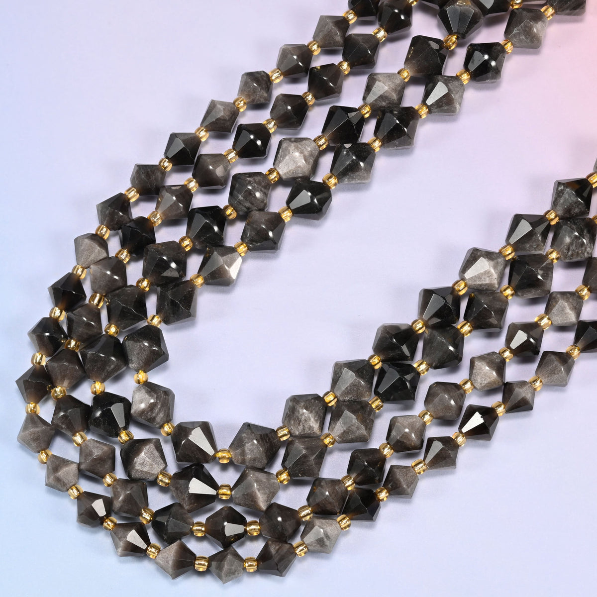Silver obsidian bicone beads in a wide loop curving down and back, charcoal and pewter tones shifting across the strand.