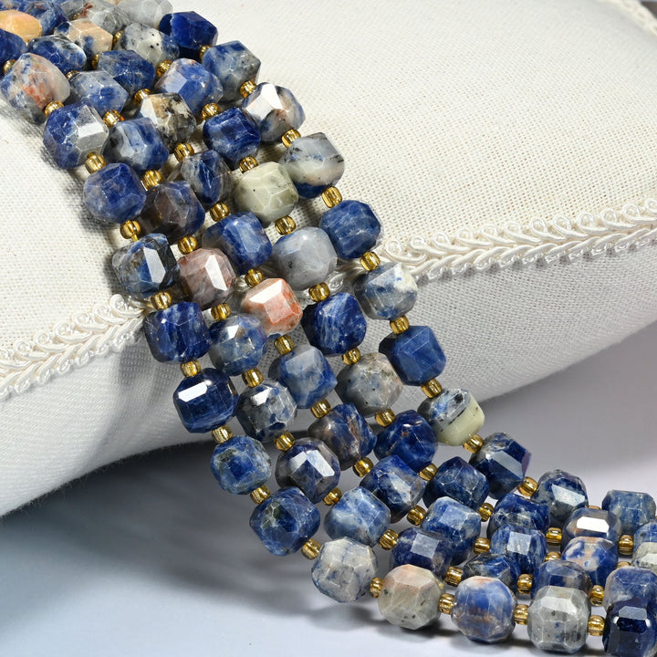 Orange sodalite faceted cube beads 6mm and 8mm with small gold spacer beads, several strands draped over a white cushion
