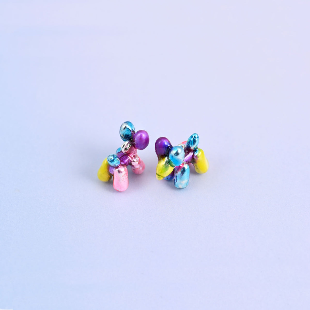 Balloon dog charms from above, the four twisted legs in yellow, pink and blue metallic enamel.