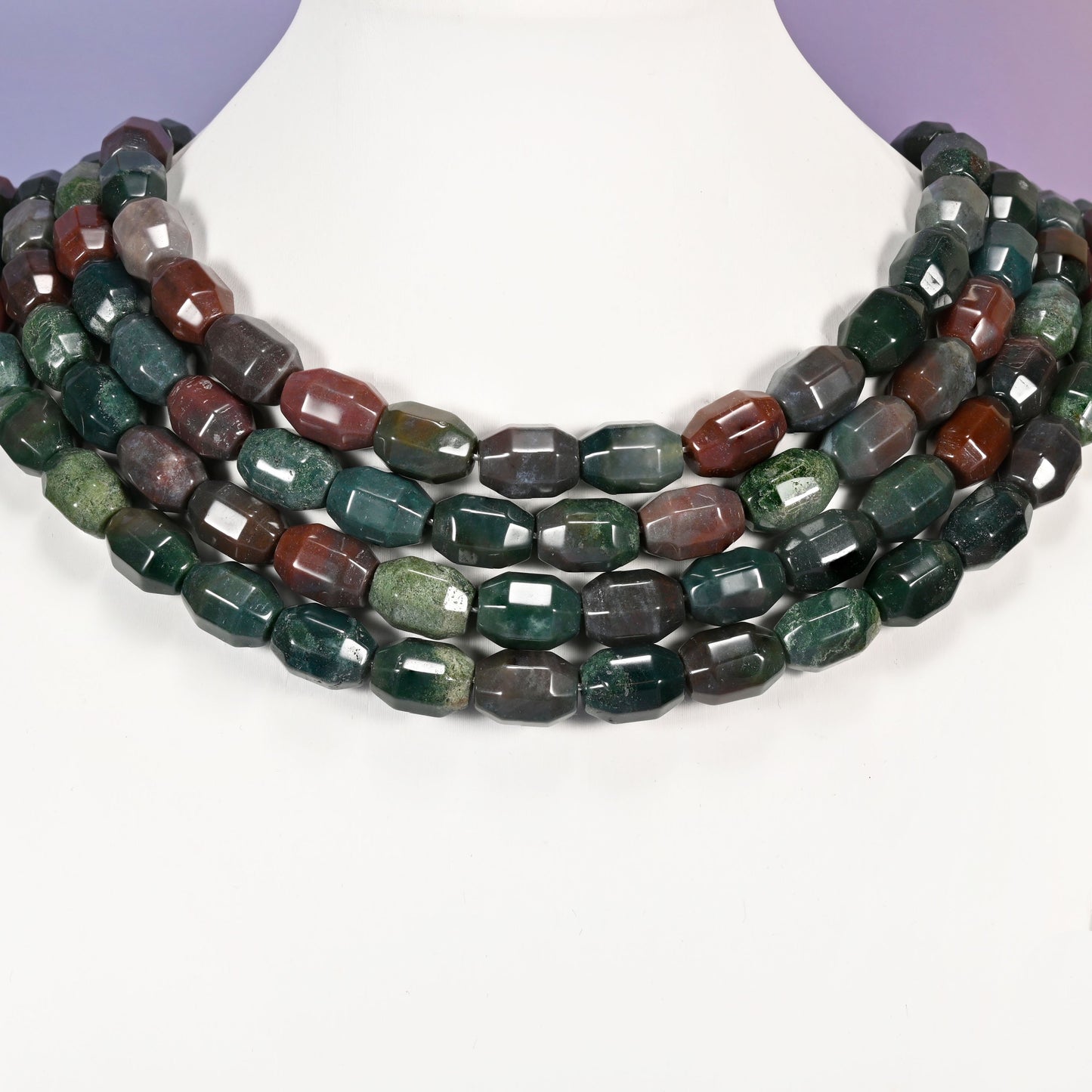 Multi-strand necklace of Indian Agate faceted barrel beads laid on a white mannequin neck form against a lavender background.