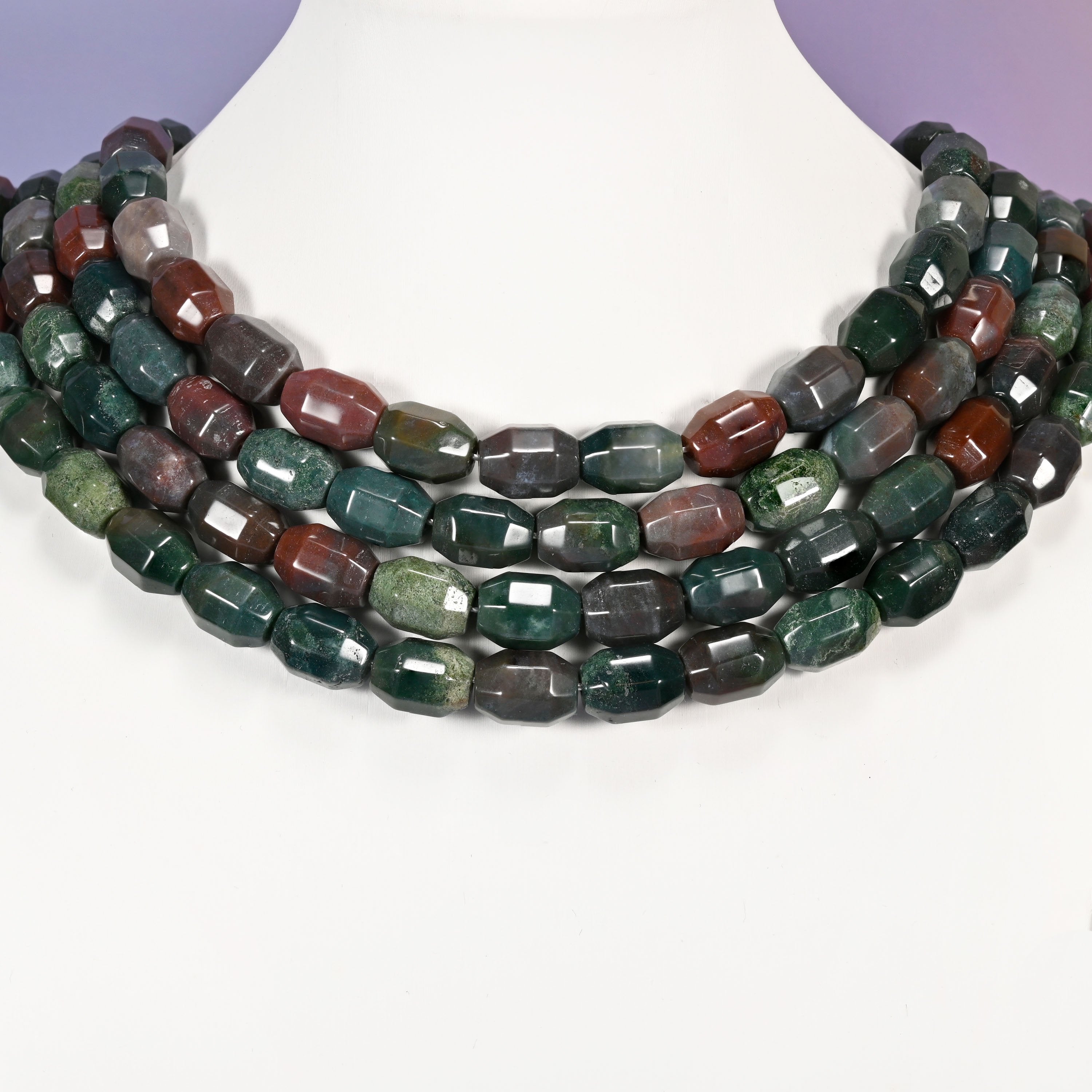 Multi-strand necklace of Indian Agate faceted barrel beads laid on a white mannequin neck form against a lavender background.