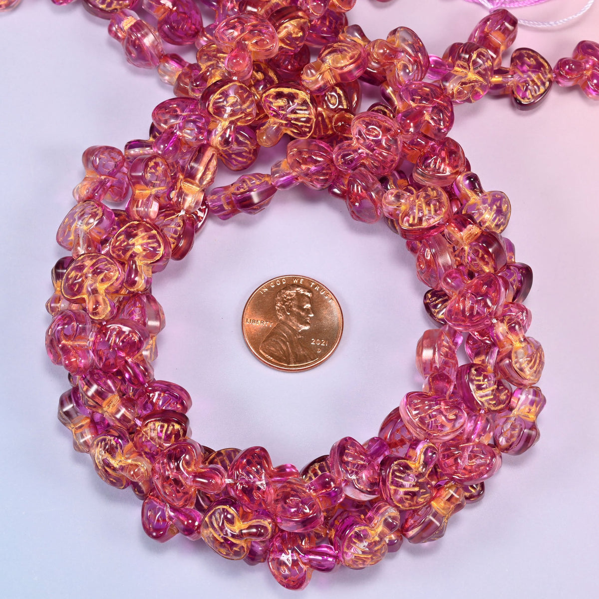 Pink gold flat mushroom glass beads coiled into a tight spiral, the strand end trailing off the top corner.