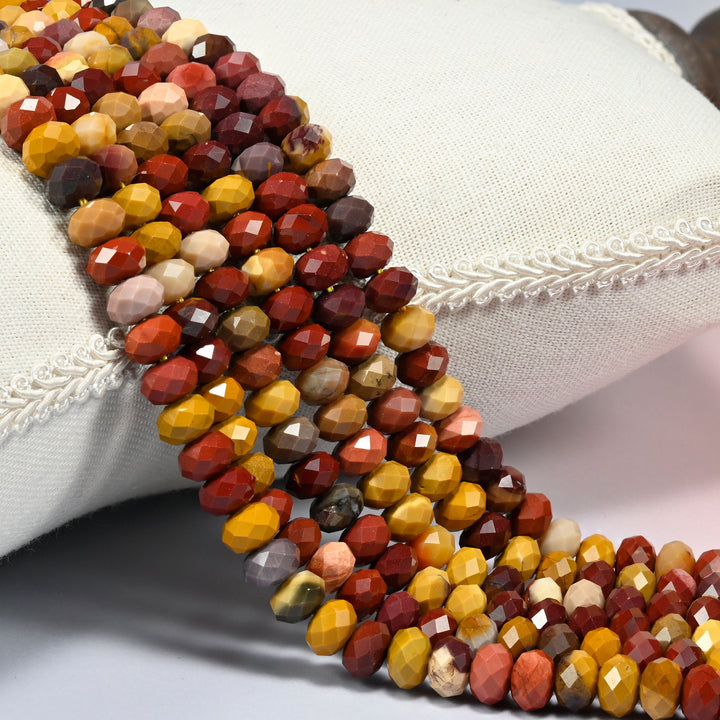 Mookaite jasper faceted rondelle beads 5x8mm draped over a linen cushion with a scalloped edge, warm yellow and brick red.