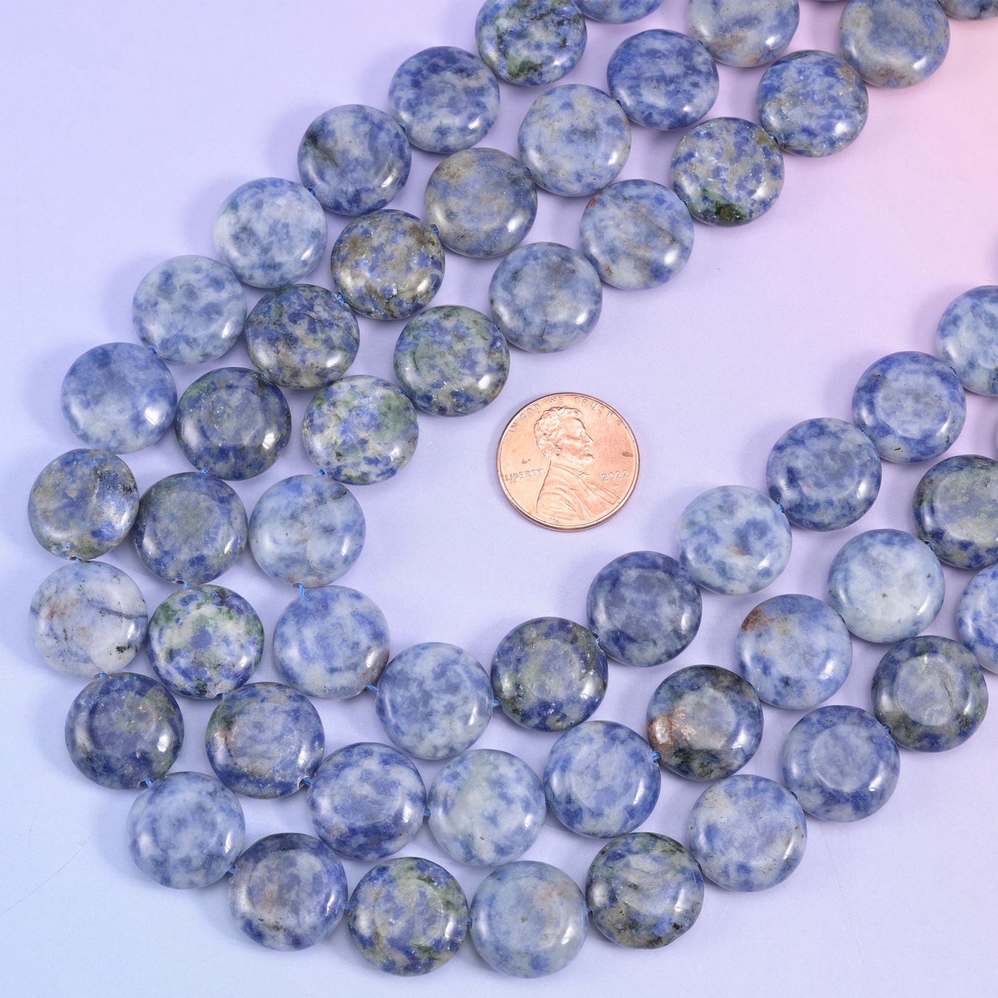 A US penny beside looped blue spot jasper coin strands, showing the 15mm disc size