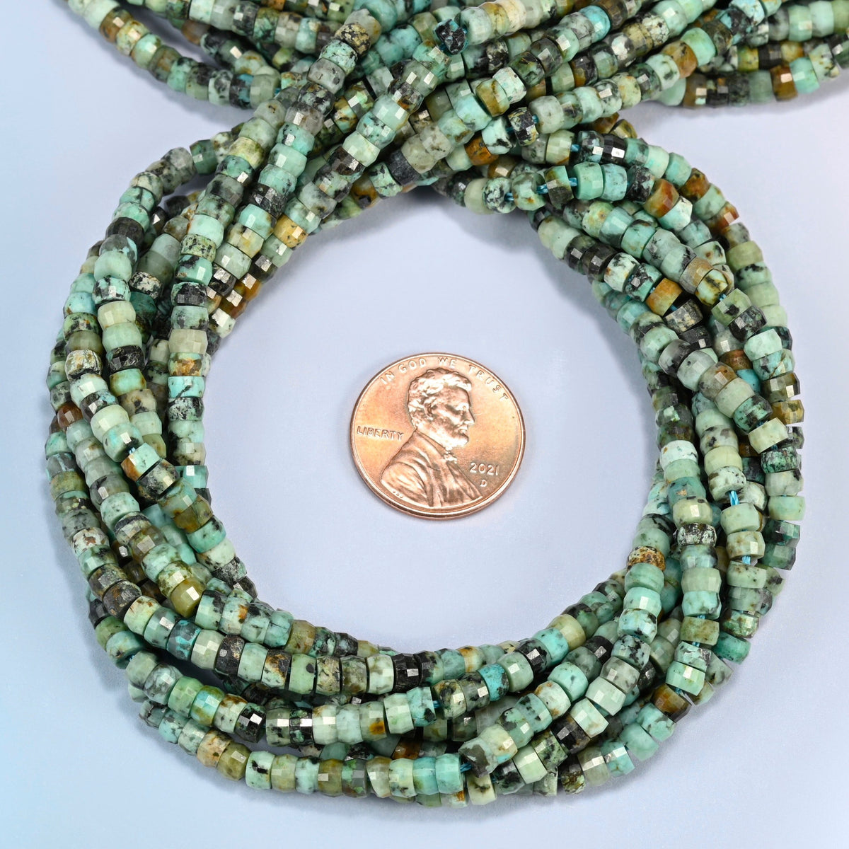 African howlite faceted heishi disc beads 2x4mm coiled in a loop around a US penny for scale, close-up of the faceted disc shape