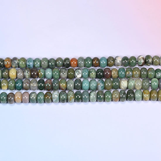 Overhead view of several rows of Indian Agate rondelle beads showing the multicolor green and rust patterning on a light lavender surface.