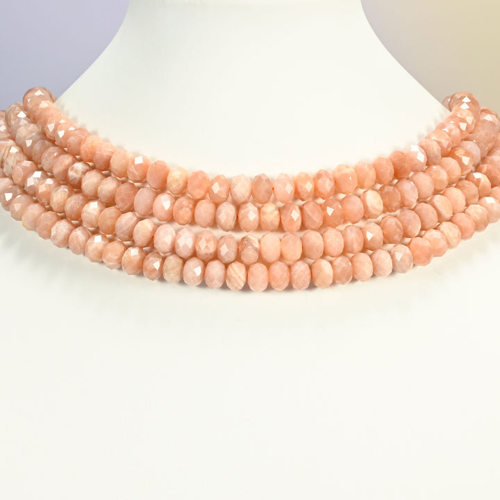 Peach moonstone faceted rondelle strands arranged as a layered collar on a white display bust, soft peach tones across the neck