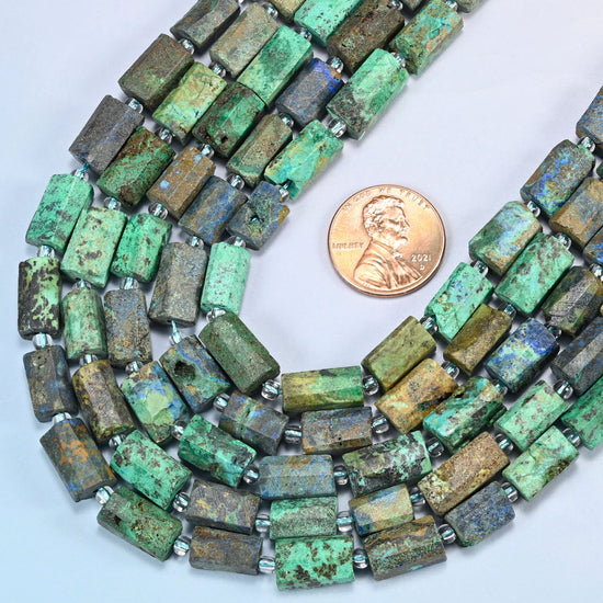 Close view of azurite chrysocolla faceted tube strands curving beside a US penny for scale, showing the raw surface with a matte feel