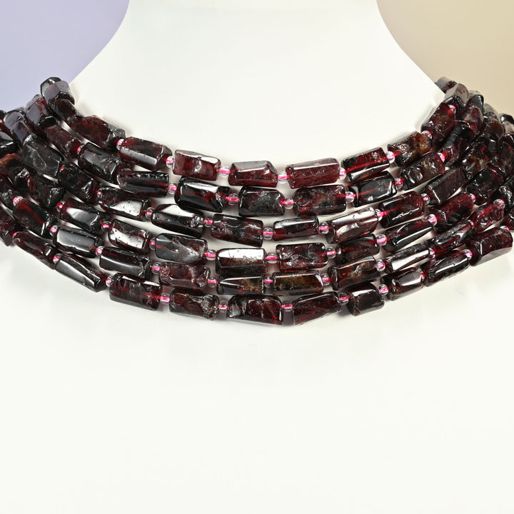 Red garnet tube strands arranged as a layered collar on a white display bust, deep cherry red beads across the neck