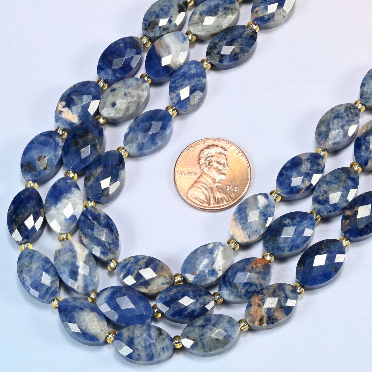 Close view of orange sodalite faceted flat oval strands curving beside a US penny for scale