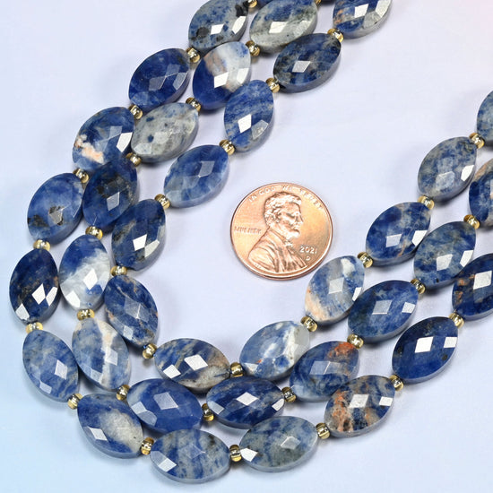 Close view of orange sodalite faceted flat oval strands curving beside a US penny for scale