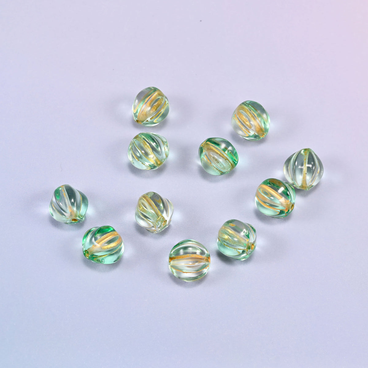 A scattered group of loose 8mm green gold pumpkin glass beads, showing the melon ribs and the drill holes.