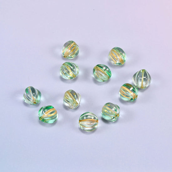 A scattered group of loose 8mm green gold pumpkin glass beads, showing the melon ribs and the drill holes.