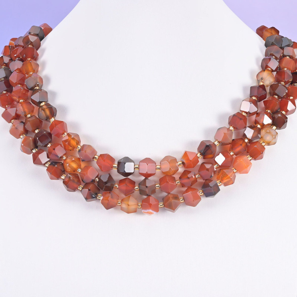 Faceted 8 sides diamond rhombus beads in dyed red strip agate on a white neck display, three strands of orange red.