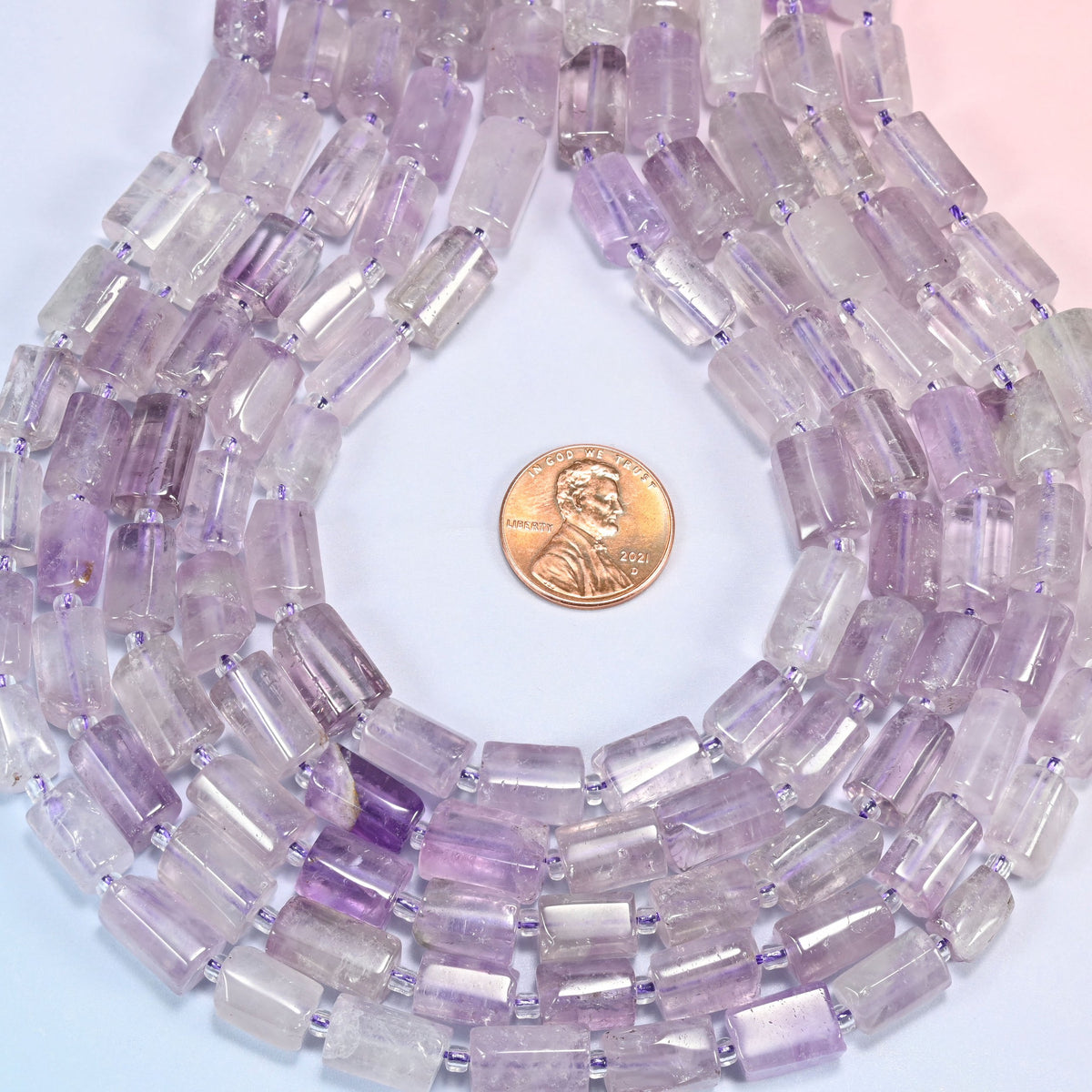Lavender amethyst faceted tube strands curved into a teardrop loop with a US penny at the center for scale.