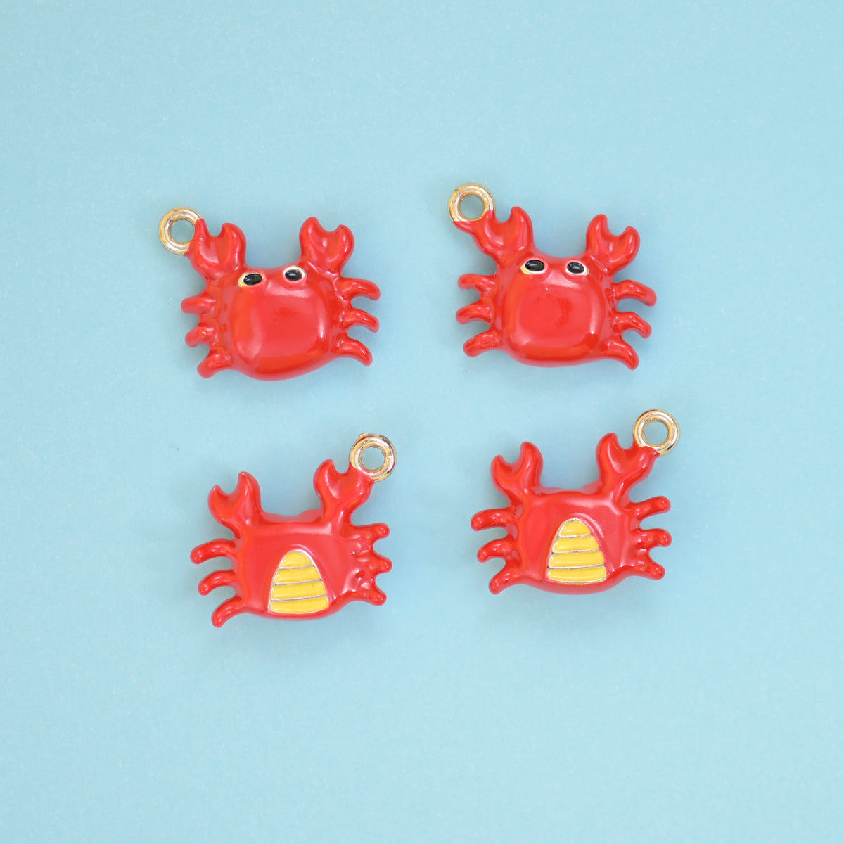 Enamel crab charms in red, front view with black eyes and reverse view showing the yellow striped belly